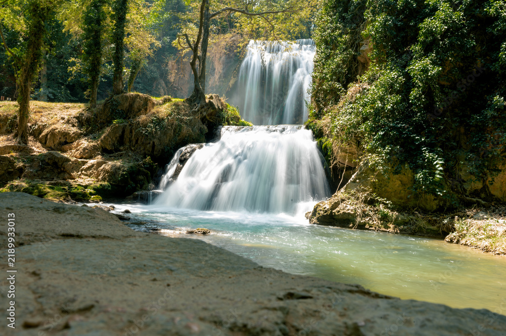 Obraz premium A waterfall cascades over rock ledges surrounded by greenery in the Monasterio de Piedra natural park in Aragon, Spain, a soft long exposure of silky white water and a turquoise pool.