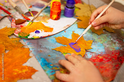 Child painting autumn maple leaf with purple paint close up