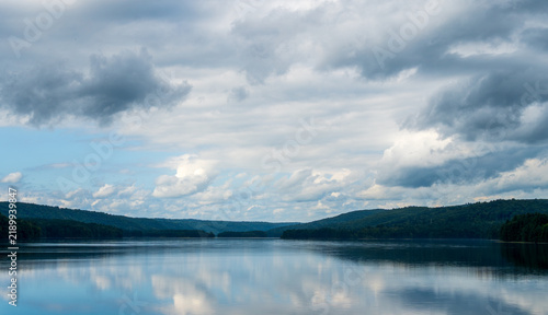 Serene mountain lake reflecting dramatic clouds and forested hills