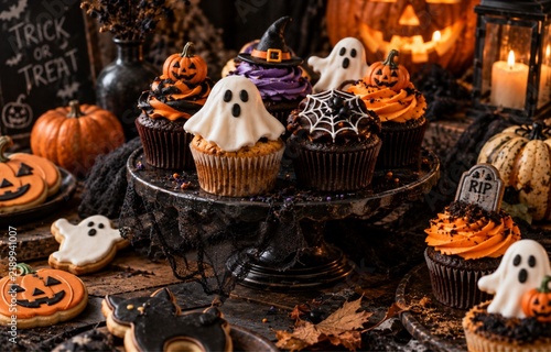Halloween cupcakes with ghost decorations, pumpkins and candles on a dark festive table