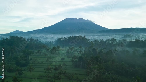Mount Agung Volcano over Misty Rice Fields at Dawn Aerial View