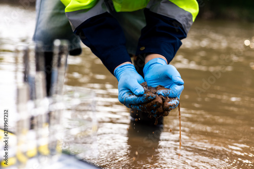 Fotografía Field worker collecting muddy riverbed sediment to test for toxic pollutants and heavy metal contamination