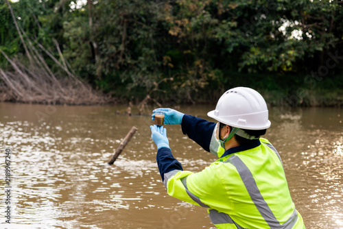 Environmental technician collecting river sediment sample for contaminant and heavy metal analysis.