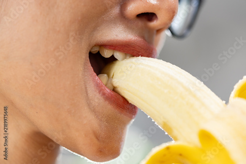Close up mouth eating peeled banana with visible teeth and glasses, healthy snack captured in colorful detail for nutrition and lifestyle concept