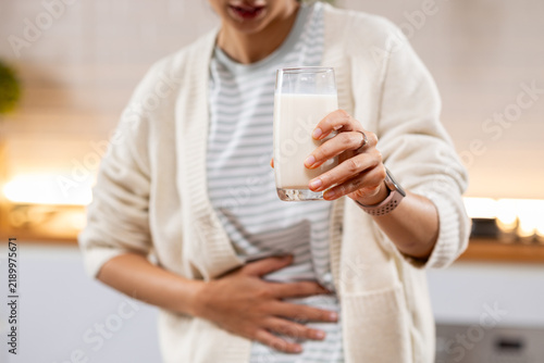Woman holding milk glass while touching stomach with discomfort at home, suggesting digestive sensitivity, lactose intolerance, abdominal pain, and nutrition concern