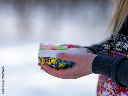 Fotografía Person holding a colorful Easter egg filled with assorted candy outdoors in a snowy winter setting, combining traditional Easter treats with a Nordic spring landscape