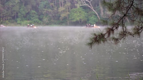 Pang Ung in Pang Tong Reservoir by focus pine needles and blur tourists people rafting in cool mist or fog floating above lake or river water in morning background at Mae Hong Son in Asia Thailand