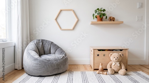 Cozy minimalist children room interior with grey bean bag chair, wooden toy chest, teddy bear, and hexagon shelf on white wall, bright scandinavian nursery design concept