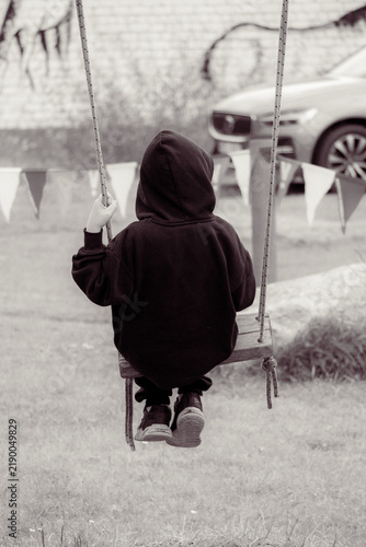 Foto Child in hoodie sitting alone on a swing seen from behind