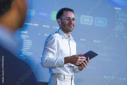 Obraz na plátne A male innovation lead dressed entirely in white holding a black tablet smiles b