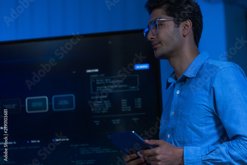 фотографія A smartly dressed male engineer in a navy blazer at his monitors moves quickly b