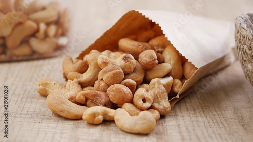 A paper bag filled with cashews tips over, and the nuts scatter across the table