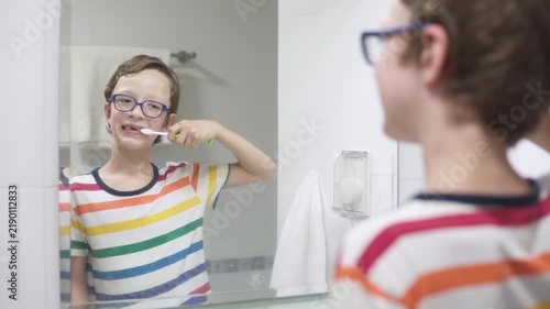 Boy in glasses is brushing his teeth at a bathroom