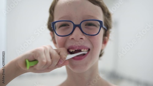 Boy in glasses is brushing his teeth at a bathroom