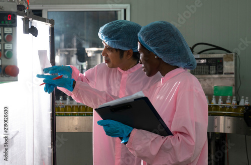 Asian male and black woman factory workers monitoring cold drink bottles on production line at drinks production plant.