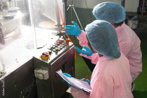 Asian male and black woman factory workers monitoring cold drink bottles on production line at drinks production plant.