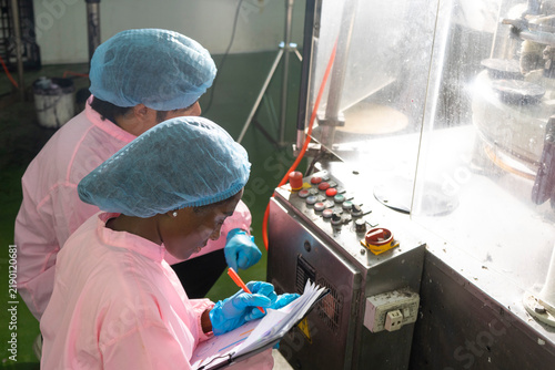 Asian male and black woman factory workers monitoring cold drink bottles on production line at drinks production plant.