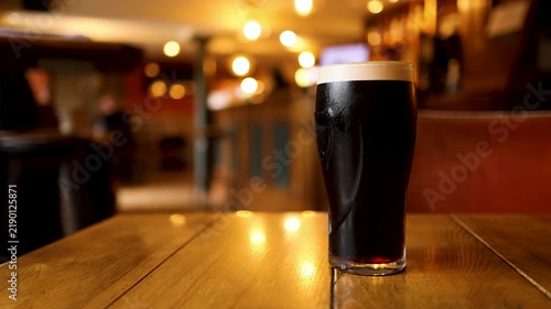 Two pints of stout beer with creamy foam head being taken from a rustic wooden table in a traditional irish pub.