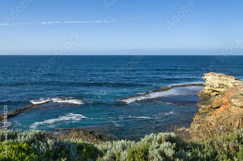 Rugged coastal landscape with coastal vegetation, rugged cliffs and natural rock pools at high tide under blue sky, at the coast of Great Otways National Park, Victoria, Australia
