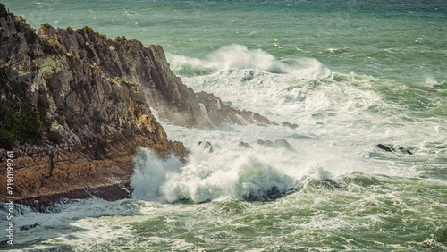 Принти на полотні Rough surf crashes into a rugged, rocky headland on a windy day with sea spray being blown off the turbulent waves along the coastline in Twofold Bay at Eden in New South Wales, Australia
