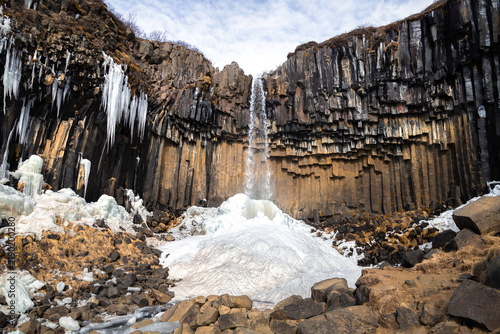 Svartifoss waterfall surrounded by basalt columns and ice formation in Skaftafell, Iceland