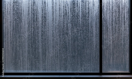 Heavy rain streaks down a glass window pane in a moody modern office