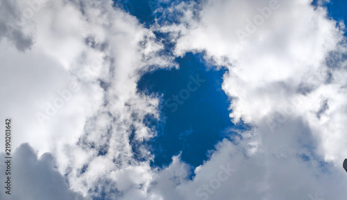 Bild auf Leinwand Wide angle view of fluffy white clouds framing deep blue sky opening
