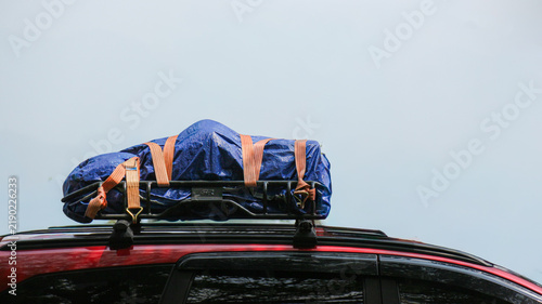 Blue waterproof cargo bag strapped to vehicle roof rack for road trip.