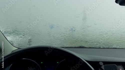 Car interior facing rain soaked windshield during heavy storm with blurred road view and dashboard in foreground