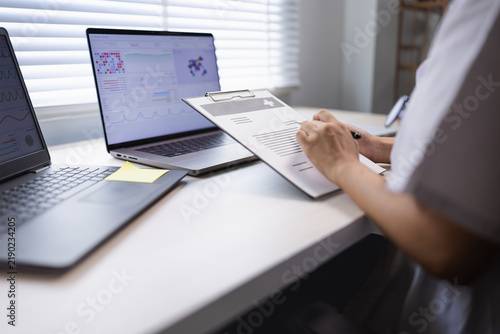 A professional medical researcher or doctor analyzing patient data charts and health statistics on laptop screens in a modern hospital office.