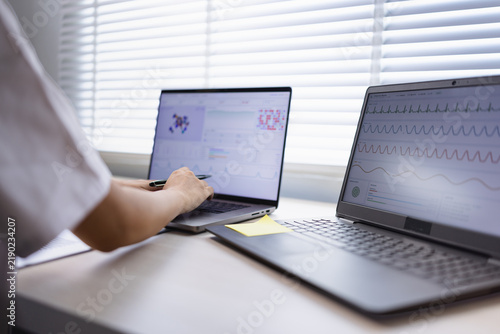 A professional medical researcher or doctor analyzing patient data charts and health statistics on laptop screens in a modern hospital office.