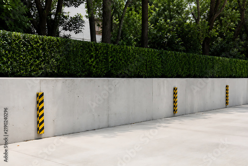 Concrete retaining wall with yellow and black striped safety bumpers along a paved surface