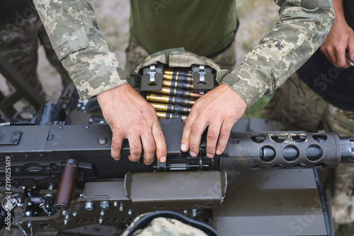 Foto Close up view of a soldier in camouflage uniform using both hands to load a linked ammunition belt into a mounted heavy machine gun