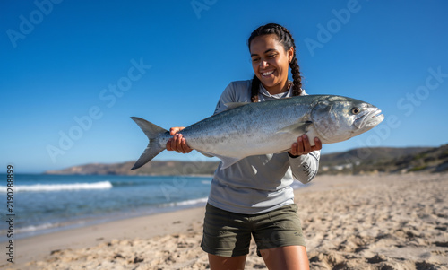 Smiling female angler proudly showing large fresh catch saltwater fish beach coastal shore recreational angling success hobbyist lifestyle triumph achievement exhilaration reward