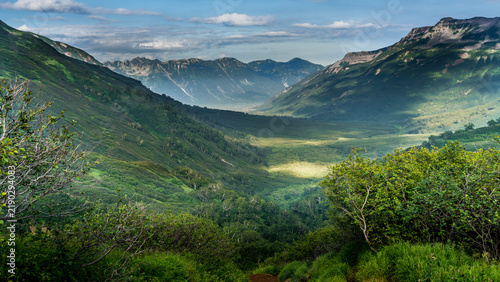 Bild auf Leinwand Beautiful Kamchatka landscape with lush green alpine meadows, colorful wildflowers, rolling volcanic hills, distant snow-capped peaks