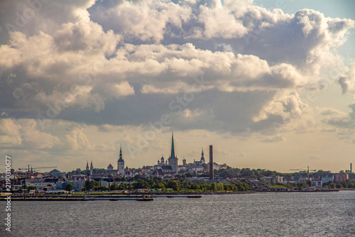 Quadro su tela A distant view of the Tallinn skyline and historic old town from the sea, captured from a ferry deck under volumetric cumulus clouds lit by warm evening sunlight