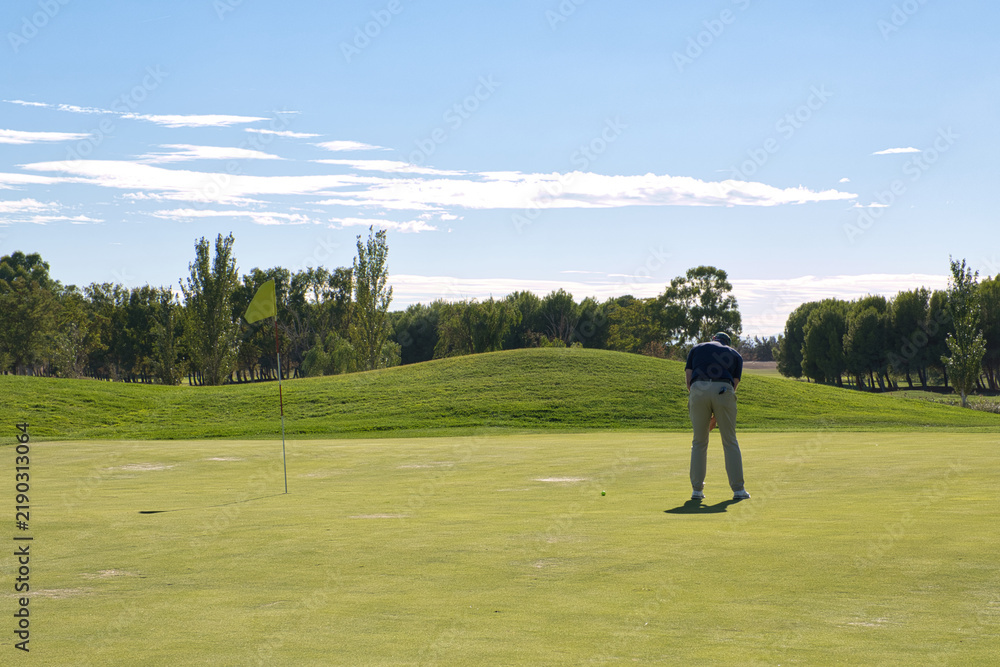 Obraz premium Golfer bending over to line up his putt near the flag, concentration and precision in a candid moment on the green.