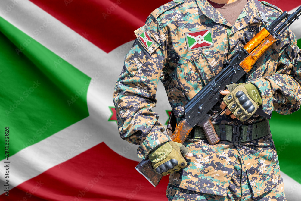 Obraz premium Burundi flag with soldier in military uniform holding assault rifle in front of it
