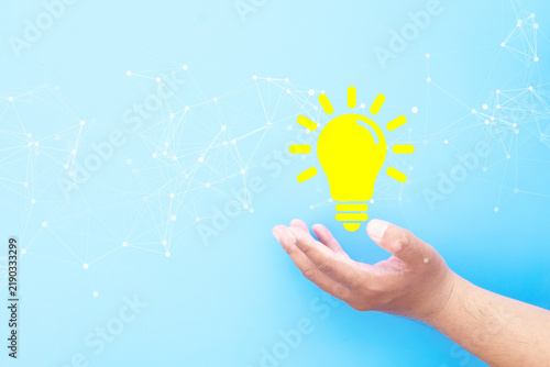 Fotografie Hand holding glowing yellow light bulb with digital network connection lines on blue background