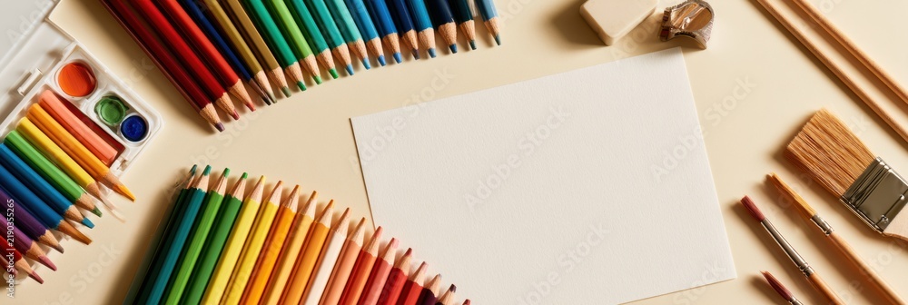 Obraz premium Bright art supplies are arranged on a cream surface, ready for children to start their creative activities using colored pencils and brushes.