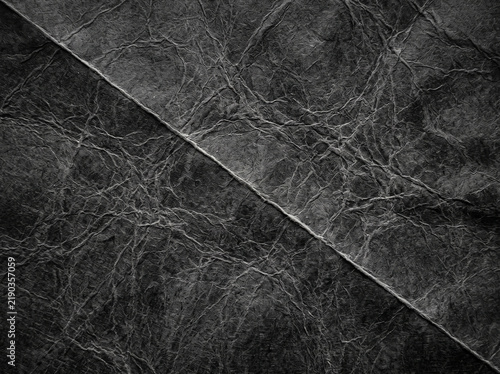 Dark textured paper background featuring folded diagonal crease and crumpled surface details