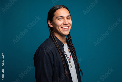 Portrait of smiling Native American young man with braided hair against blue background