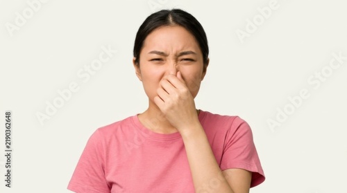 Young Asian woman pinching her nose with a disgusted expression, reacting to a bad smell or odor, isolated on a light background, concept of disgust and unpleasantness