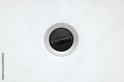 Clean Stainless Steel Sink Drain with Black Stopper on White Porcelain Surface