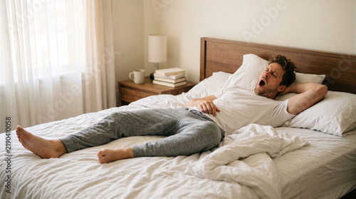 Fototapeta Man yawning widely while lying in bed with rumpled sheets