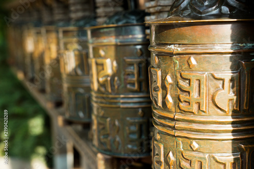 Obraz na płótnie Close-up of ornate Buddhist prayer wheels arranged outdoors in Vienna, Austria, with warm metallic textures and a softly blurred green background, suited to cultural and spiritual content