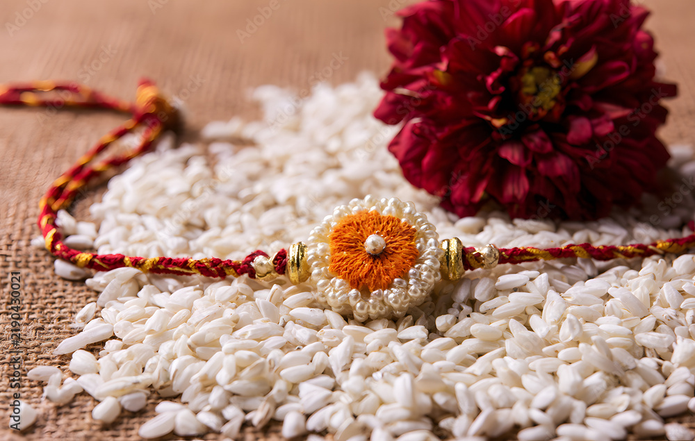 Obraz premium Raksha Bandhan is an Indian festival with beautiful Rakhi, rice grains, and flowers. It is a traditional Indian wristband that symbolizes love between sisters and brothers