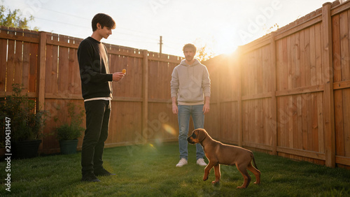 Two young men with Doberman puppy in backyard sunset