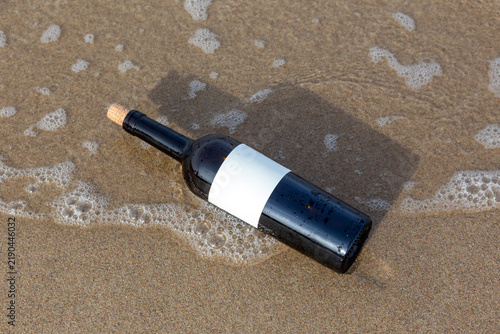 Message in a bottle with blank label on wet sandy beach
