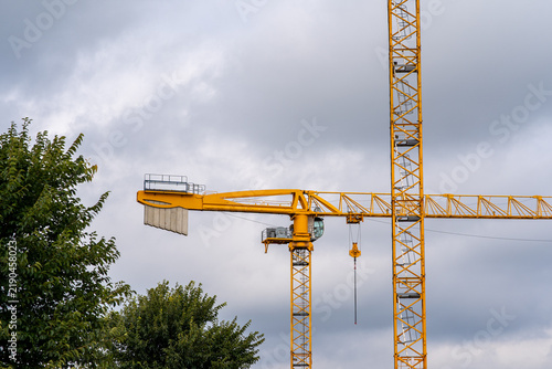 Fotografía Low angle view of two yellow tower cranes with counterweights against cloudy gra